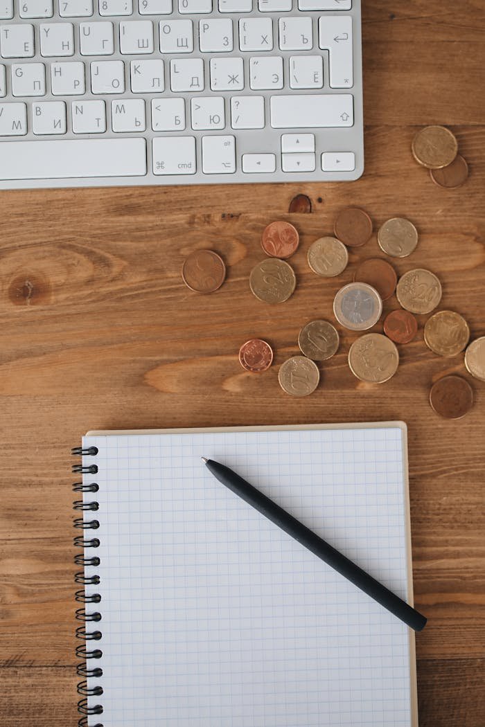 Home Overhead view of a workspace with keyboard, coins, and a notebook on a wooden desk